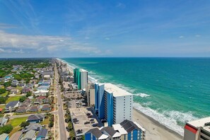 A coastal cityscape with a beachfront hotel, a wide road, and residential buildings.