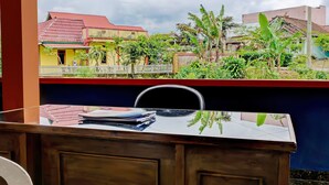 A room with a wooden desk, a chair, and a view of a residential area with houses and greenery. - OYO 92079 Anaqi Homestay Syariah (Pagar Alam)