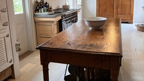 Een keuken met een houten tafel, witte kasten en een groot raam.
