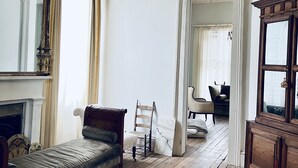 Een kamer met een houten vloer, een bed, een stoel, een open haard en een grote spiegel.
