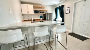 A compact kitchen with a white countertop, three white bar stools, a microwave, a refrigerator, and a sink. - 1-bedroom in Fort Lauderdale w/FREE Parking,Kitchen,Patio-8mins from FLL Airport (Fort Lauderdale)