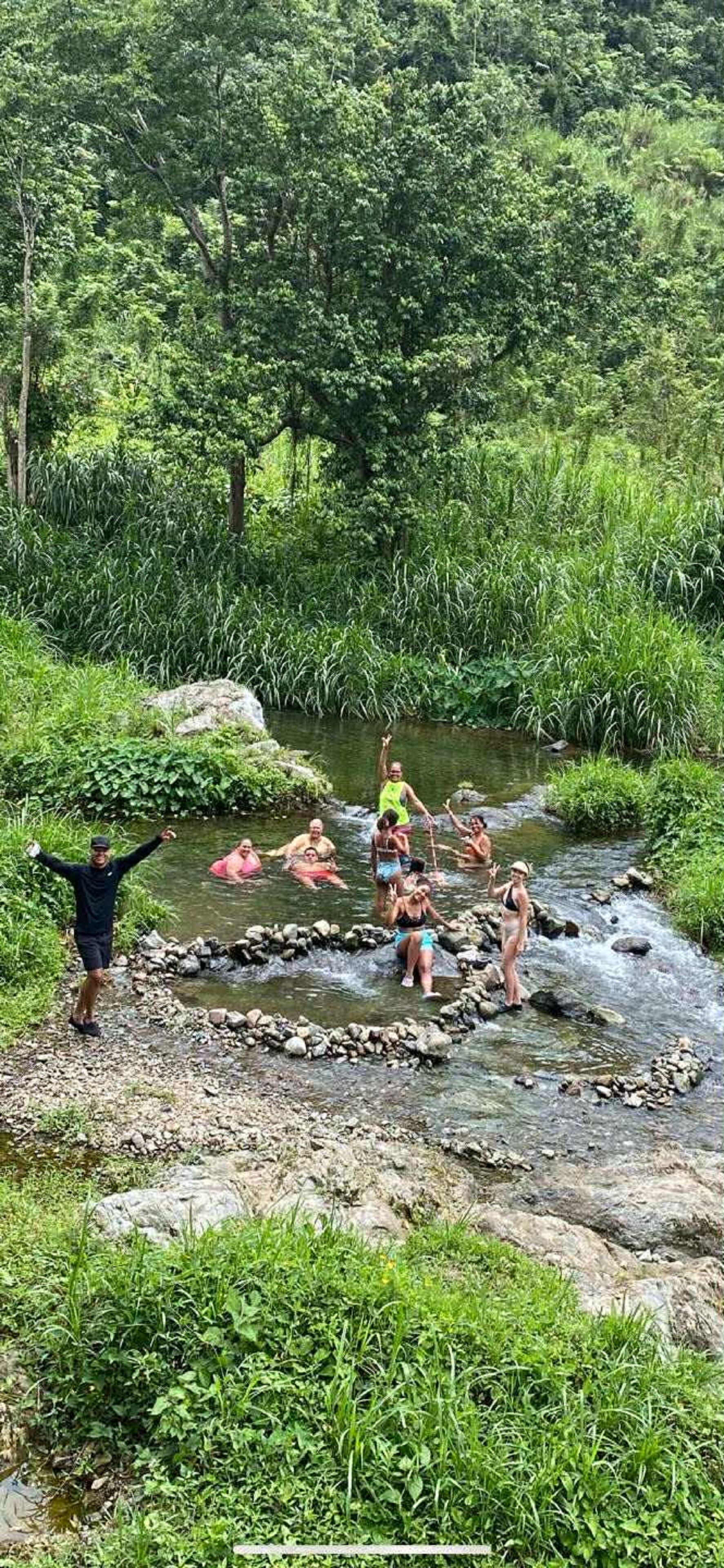 A group of people enjoying a natural water body surrounded by lush greenery.