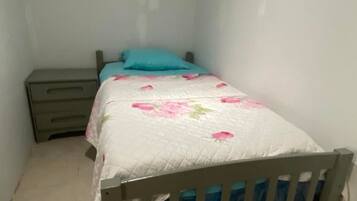 Una habitación pequeña con cama individual, cabecera de madera, mesita de noche y colcha estampada con motivos florales.