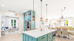 A modern kitchen with teal cabinetry, a white island, and pendant lighting. - Pura Vida Villa: Luxury Coastal Retreat With Private Heated Pool (Murrells Inlet)