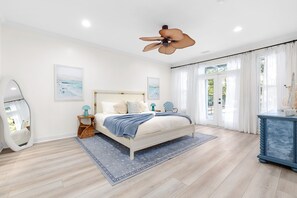 Une chambre à coucher avec un lit, un ventilateur de plafond, un grand miroir et une vue sur l’extérieur par une fenêtre.