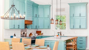 A kitchen with teal cabinetry, a central island, wicker chairs, and pendant lighting. - Pura Vida Villa: Luxury Coastal Retreat With Private Heated Pool (Murrells Inlet)