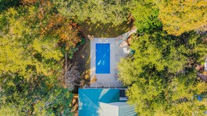 Vue aérienne d’une maison avec une piscine, entourée d’arbres.