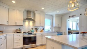 A modern kitchen with white cabinetry, a central island, and a stove. - Stone Harbor Bar on the Bay (Middle Township)