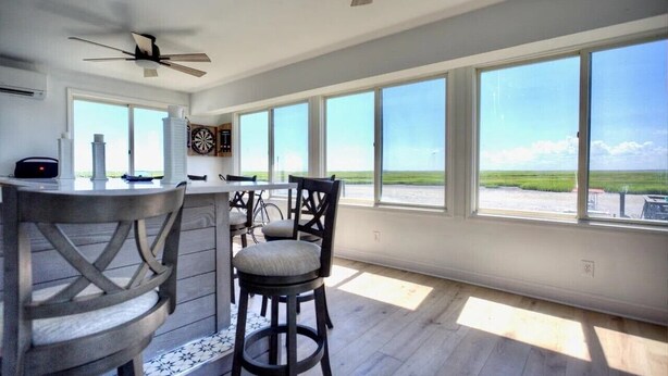 A spacious kitchen with large windows, a ceiling fan, and a dining area with bar stools. - Stone Harbor Bar on the Bay (Middle Township)