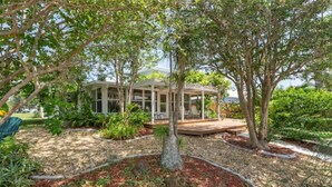 A covered outdoor area with a wooden deck, surrounded by trees and a garden. - Long-Term Discount!Unique 3BR canal home, Private Dock, Boat Lift, Deck! (Punta Gorda)