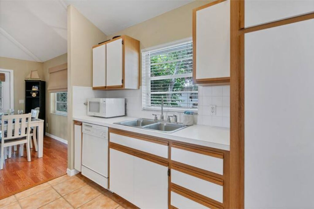 A modern kitchen with white cabinets, a microwave, a sink, and a window with blinds.