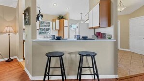 A modern kitchen with a central island, two bar stools, and a view of the living area. - Long-Term Discount!Unique 3BR canal home, Private Dock, Boat Lift, Deck! (Punta Gorda)