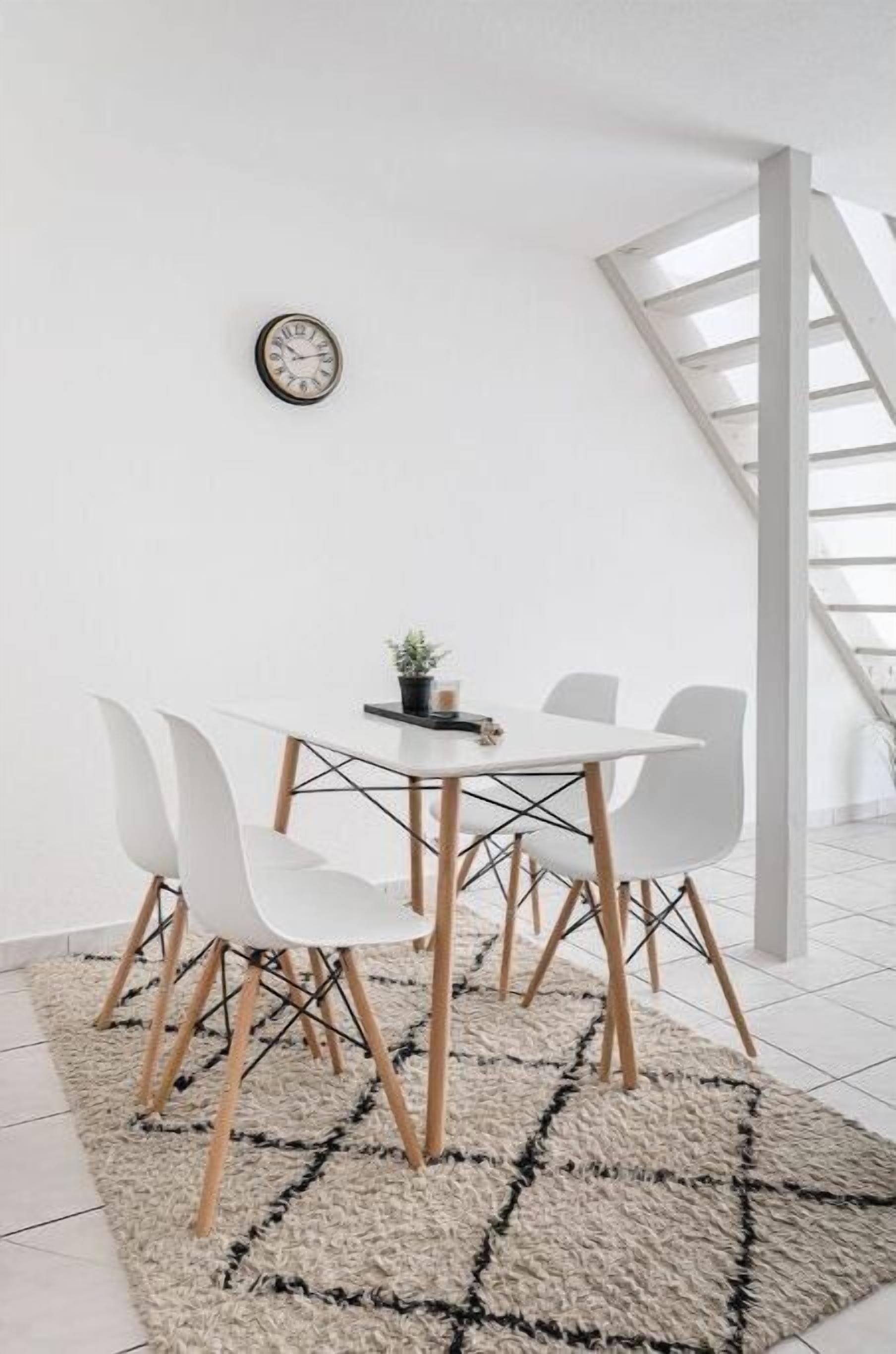 Een moderne eethoek met een witte tafel en stoelen, een klok aan de muur en een trap op de achtergrond.