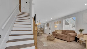 Ein modernes Wohnzimmer mit einer Holztreppe, einem beige Coloured Sofa und einem Essbereich mit einer Pendelleuchte.