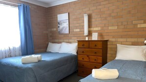 Habitación de hotel con dos camas, un tocador de madera y una ventana con cortinas azules.