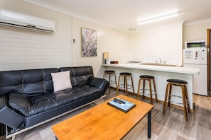 A modern living room with a black leather sofa, a wooden coffee table, and a kitchen area with a white countertop and stools.