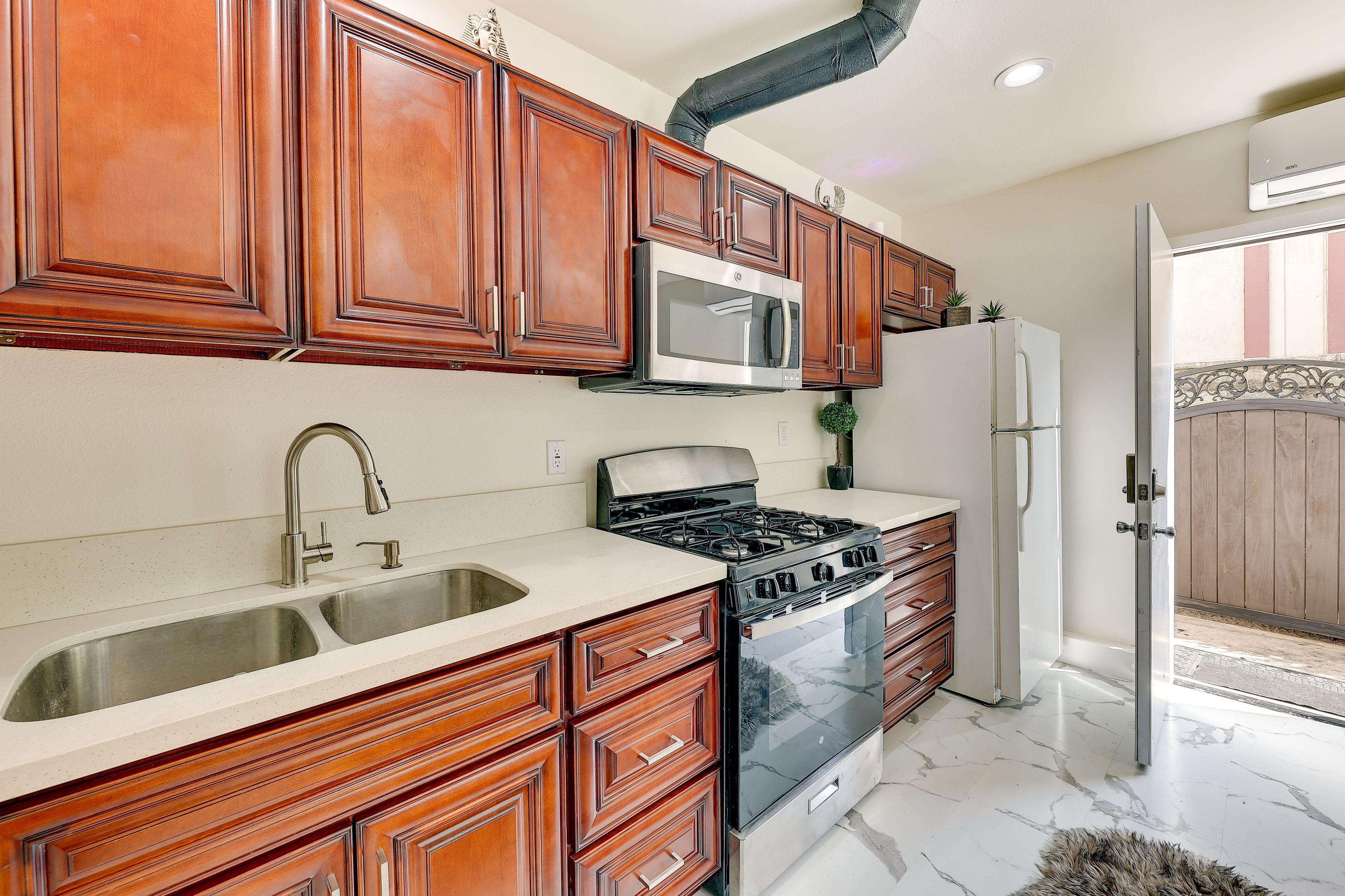 A kitchen with wooden cabinets, a stainless steel sink, a microwave, a stove, and a refrigerator.