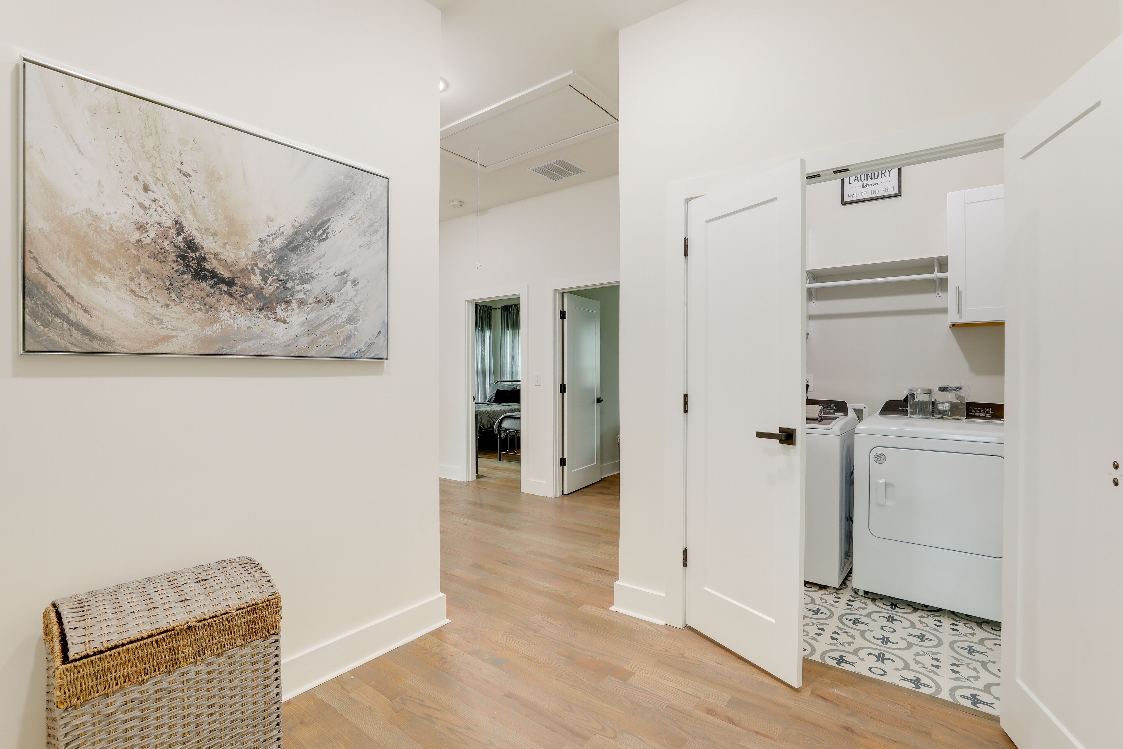A hallway with a laundry area, a wicker basket, and a painting on the wall.