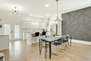 A modern kitchen with white cabinets, a central island, and a dining area with clear chairs. - Modern Decatur Home ~ 7 Mi to Atlanta! (Decatur)