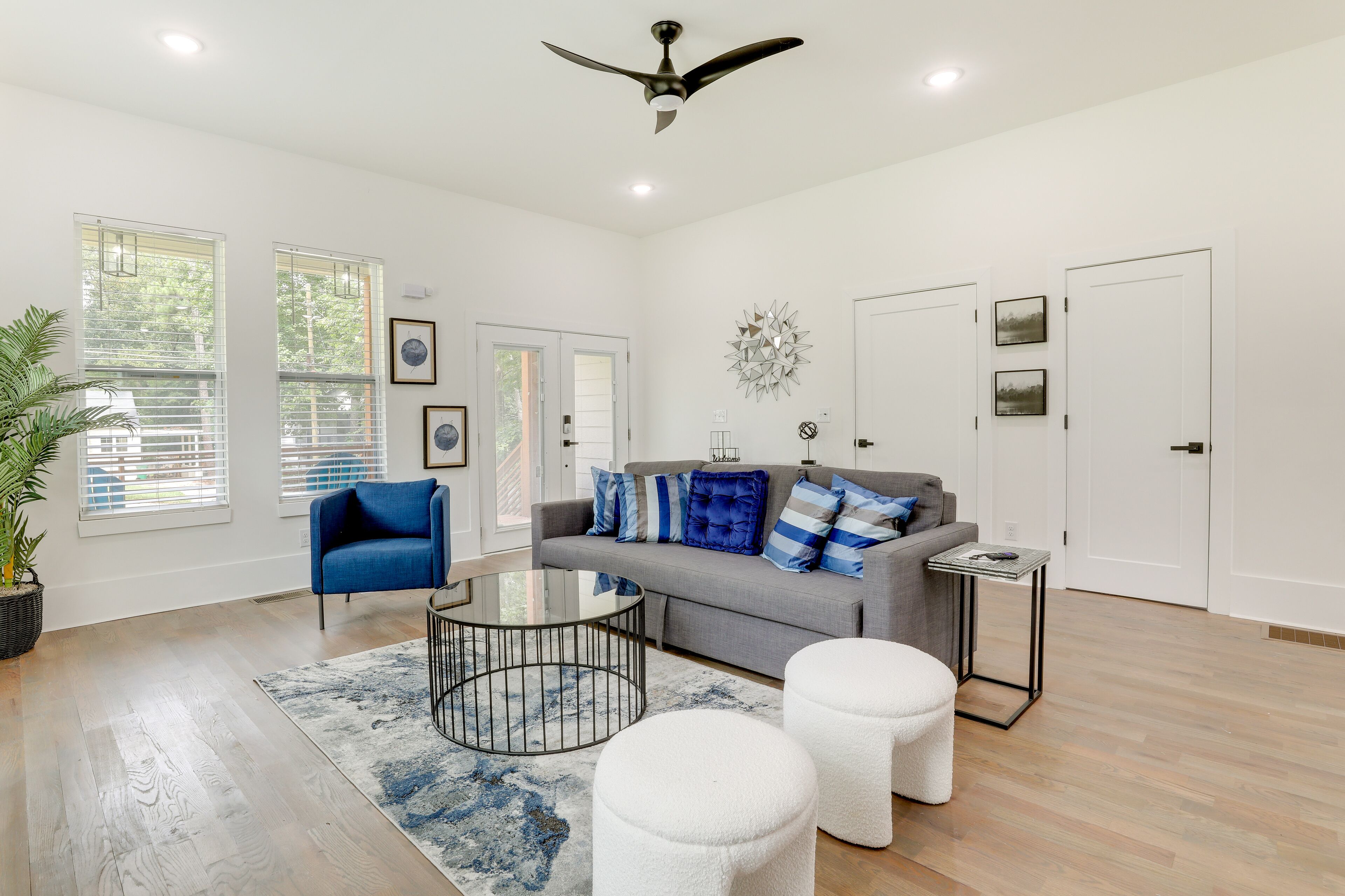 A spacious living room with a grey sofa, blue and white cushions, a round coffee table, and a ceiling fan.