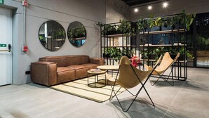 A modern lounge area with a brown leather sofa, a round coffee table, and a unique chair with a metal frame. There are two round mirrors on the wall, and a plant wall with various green plants. - The new apartment, very bright, all brand new fully equipped so that you... (Medellín)