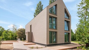 A modern two-story house with a sloped roof, large windows, and a paved patio area. - 4 bedroom stunning apartment in Tossens (Tossens)
