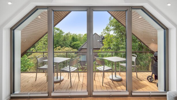 A spacious balcony with a wooden deck, large sliding glass doors, and a view of a house and trees. - 4 bedroom stunning apartment in Tossens (Tossens)