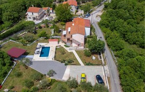 An aerial view of a residential area with a swimming pool, a red-roofed building, and a yellow car parked in a driveway. - Amazing apartment in Malinska with WiFi (Malinska)