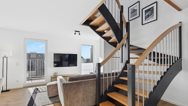 Una sala moderna con una escalera de madera, un televisor de pantalla plana y un sofá.