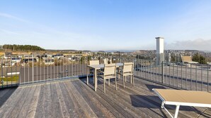Una terraza en la azotea con vistas a un barrio residencial, una barandilla de metal y una mesa con sillas.