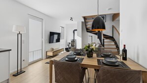 Un área de comedor moderna con una mesa de madera dispuesta para dos personas, un televisor montado en la pared y una escalera que conduce a un nivel superior.