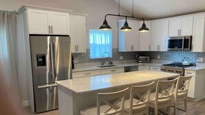 Une cuisine moderne avec des meubles blancs, des appareils en acier inoxydable et un îlot central doté de tabourets de bar.