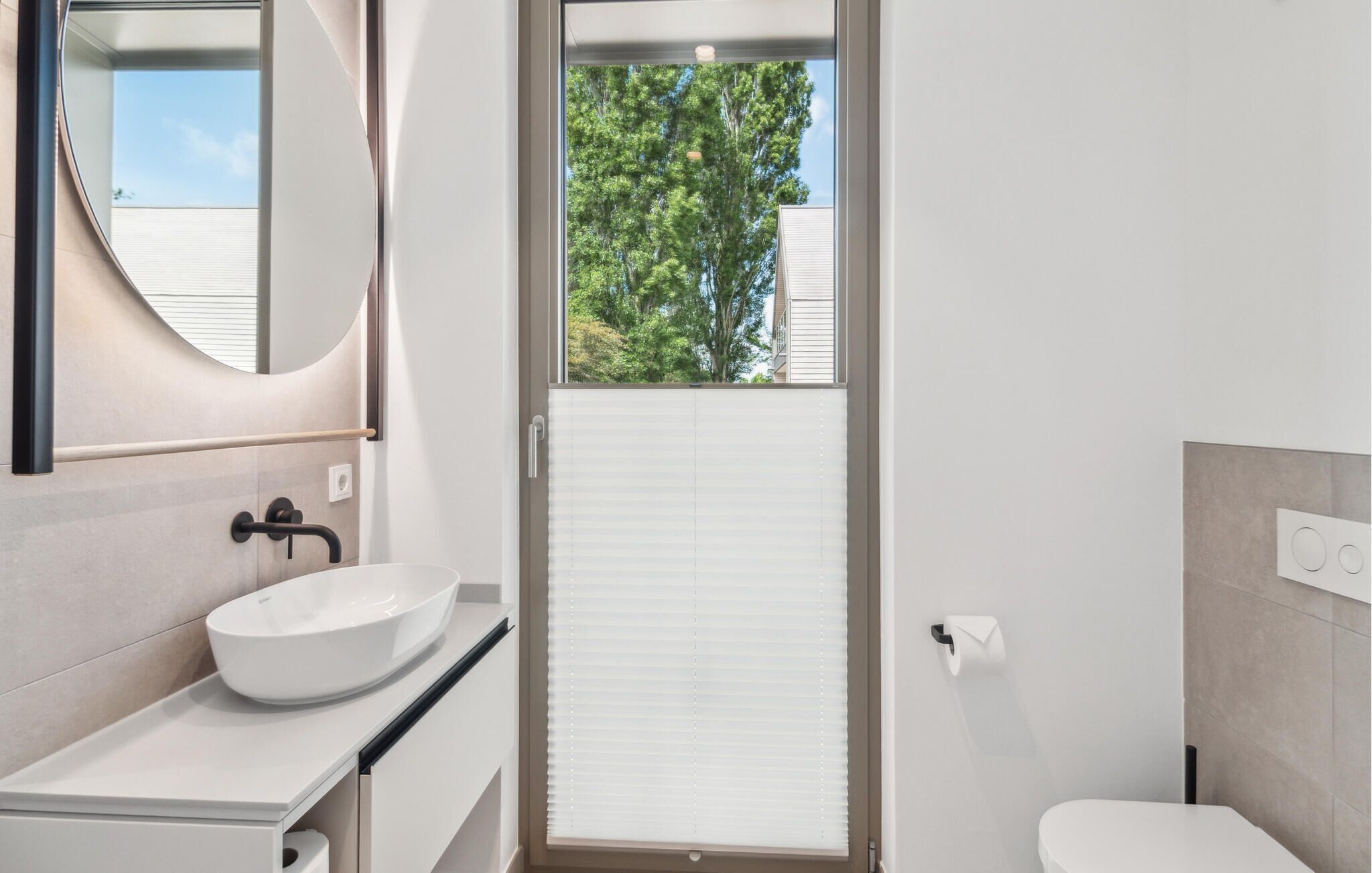 A modern bathroom with a white sink, a mirror, and a toilet.