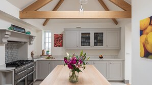 A modern kitchen with a wooden ceiling, white cabinets, a central island with a vase of flowers, and a stove.