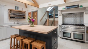 A modern kitchen with a central island, wooden stools, a RangeMaster stove, and a backsplash with geometric tiles.