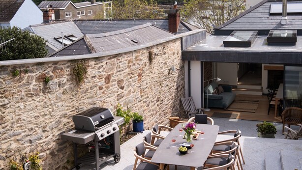 A modern outdoor patio with a stone wall, a barbecue, and a dining area with chairs and a table.