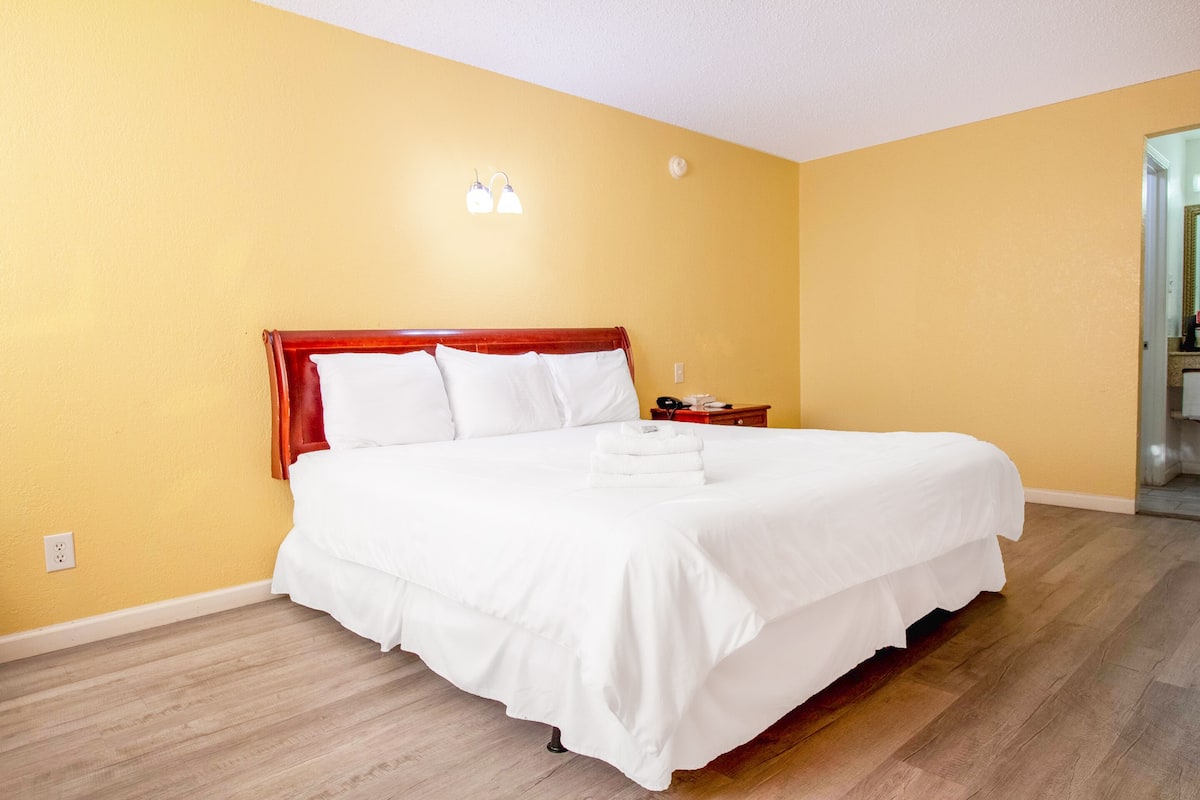 A neatly made bed with white linens in a room with yellow walls and wooden flooring.