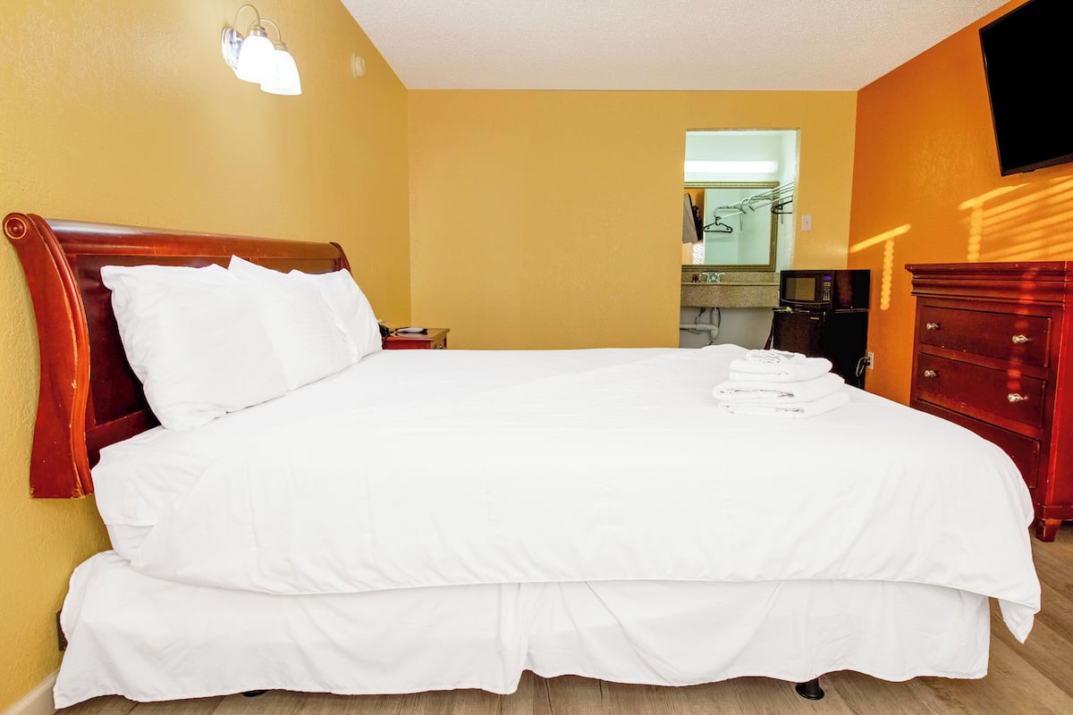 A hotel room with a large bed, a wooden headboard, a TV mounted on the wall, and a red dresser.