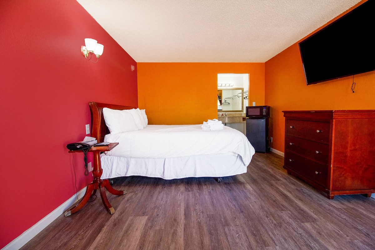 A hotel room with a bed, a dresser, a microwave, and a TV mounted on the wall.