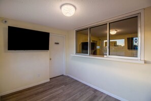 Una habitación con una televisión de pantalla plana montada en la pared, una puerta corrediza de vidrio y piso de madera.