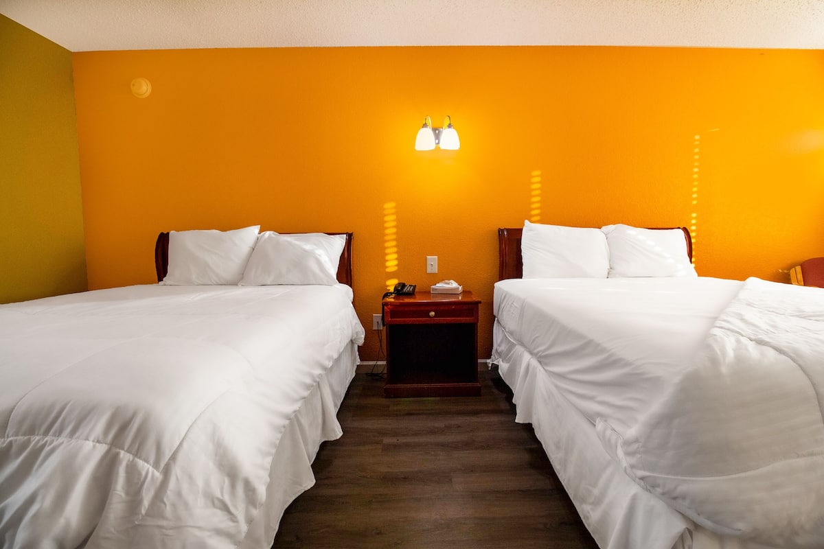 A hotel room with two beds, a wooden nightstand, and a wall-mounted light fixture.