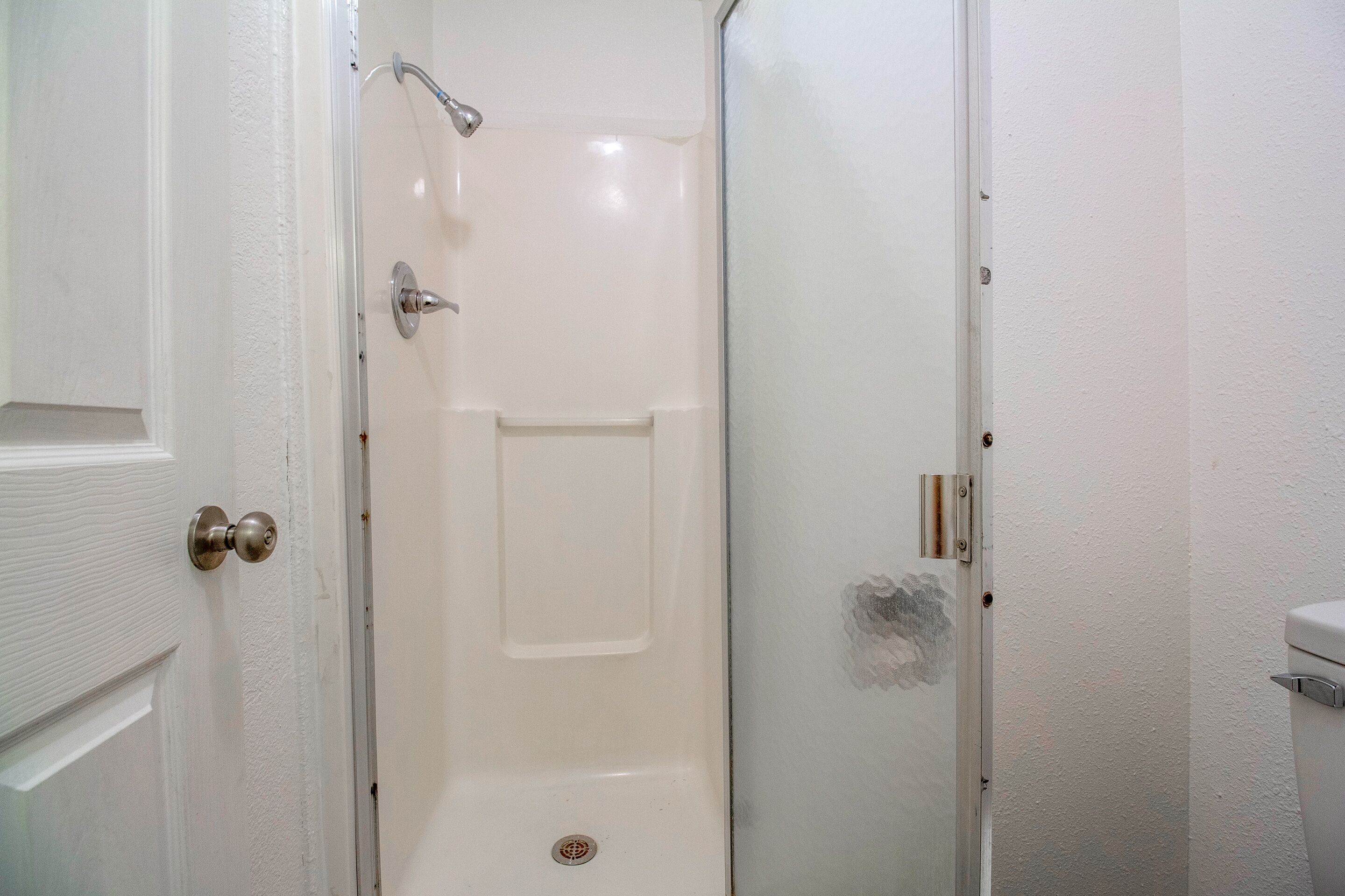 A white bathroom with a shower, a door with a round handle, and a toilet.