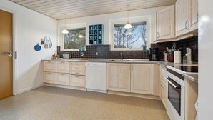 A modern kitchen with light wood cabinets, a black tiled backsplash, and a large window providing natural light.