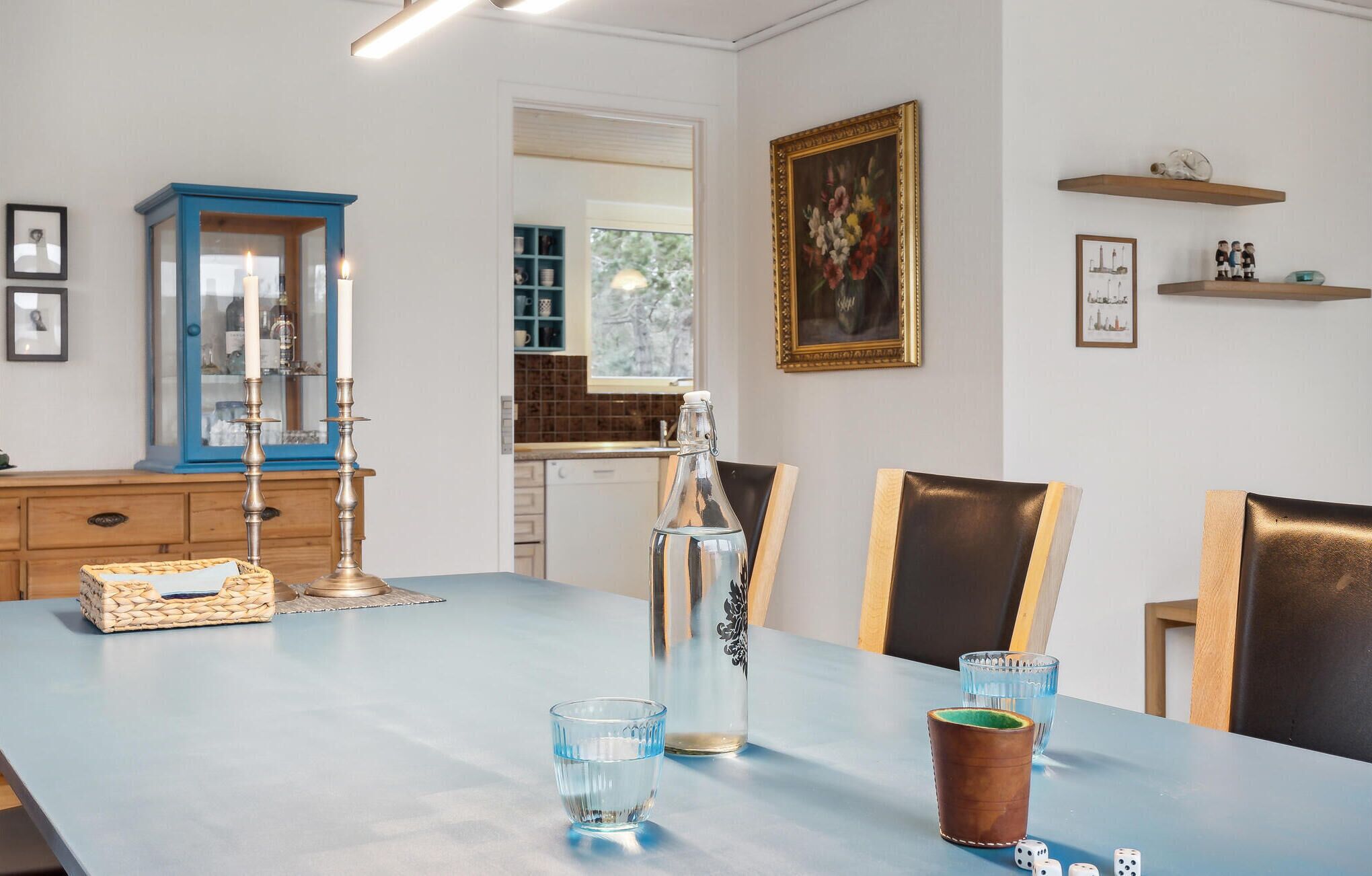 A dining area with a light blue table, chairs, a candle holder, a bottle, and glasses.
