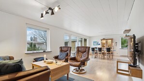 A spacious living room with a large window, a dining area with a wooden table and chairs, and a cozy seating area with a sofa and armchairs.