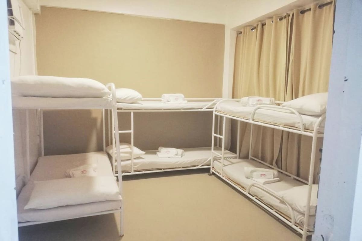 Una habitación de hotel con literas, una mesita de noche y una cortina.