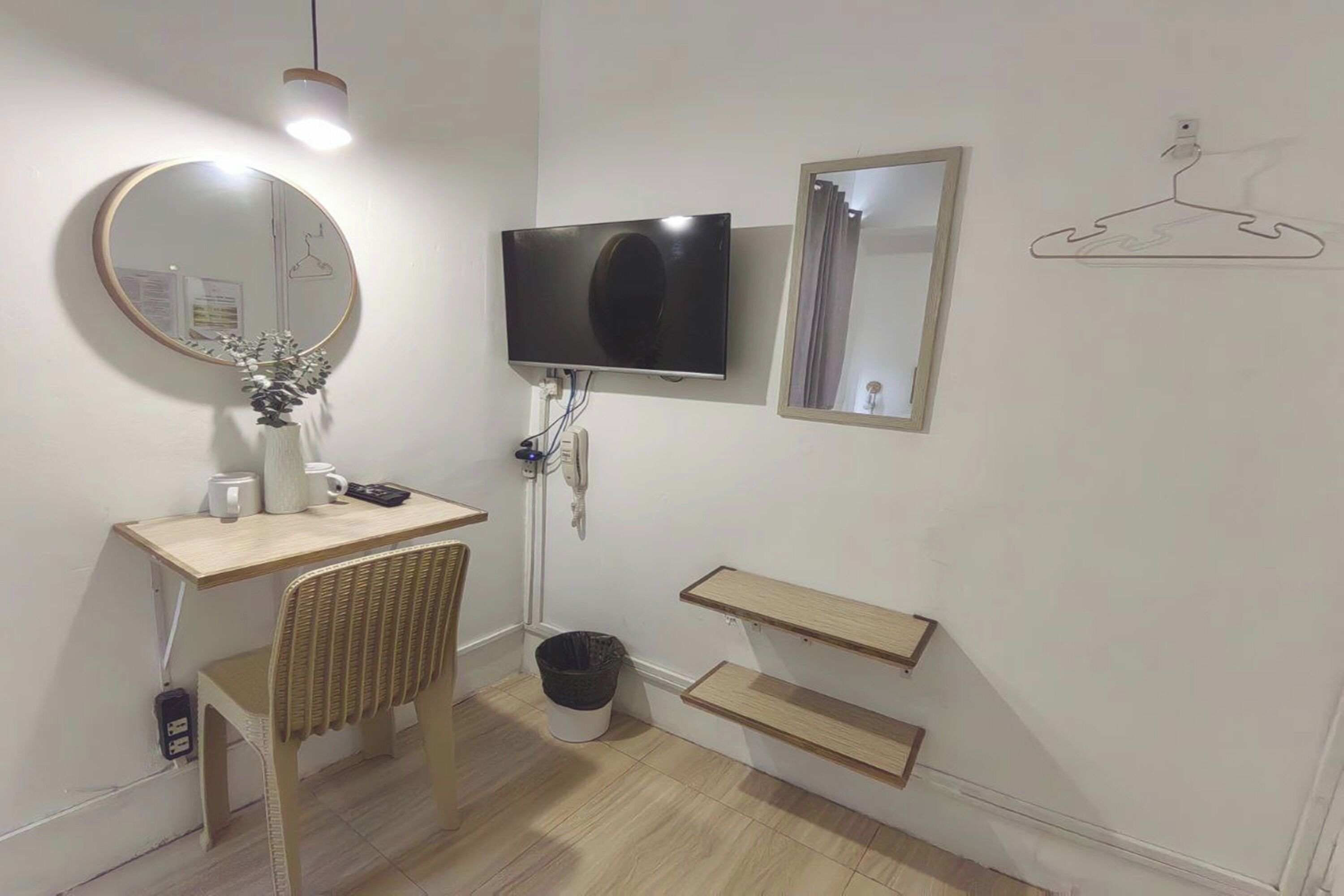 Un baño moderno con un espejo redondo, un televisor de pantalla plana, un tocador de madera y dos repisas de madera.