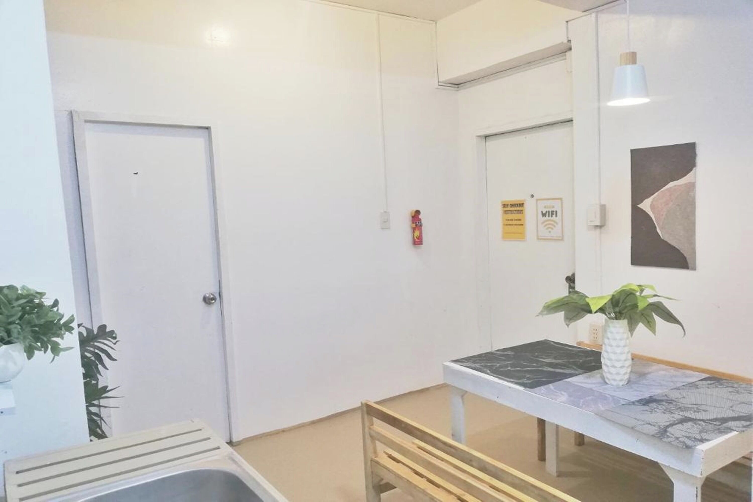 A clean, modern hallway with a white door, a small table with a plant, and a wall-mounted fire extinguisher.