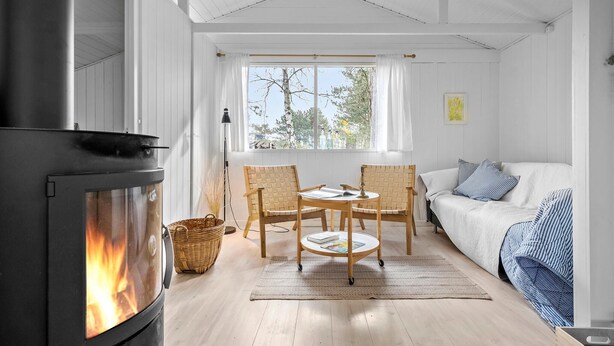 Een gezellige kamer met een open haard, een bank, een eettafel met stoelen en een raam met gordijnen.