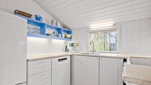 Een moderne keuken met witte kasten, een blauwe plank en een raam met uitzicht op bomen.